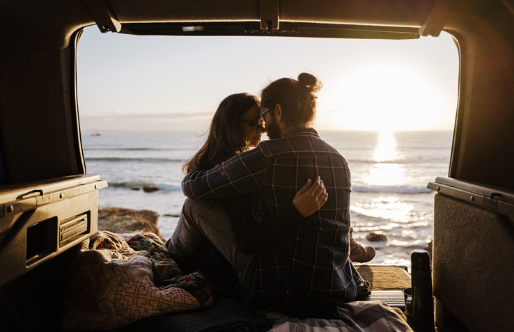 A picture of a couple embracing romantically in a van by the ocean.